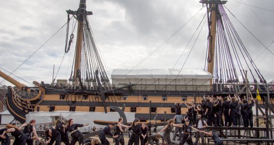 Outdoor performance of The Seafarers - dancers against a backdrop of a large ship.