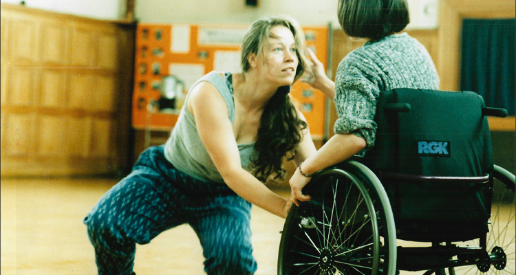 A photo of Vicki Balaam in duet with a dancer in a wheelchair who has their back to the camera.