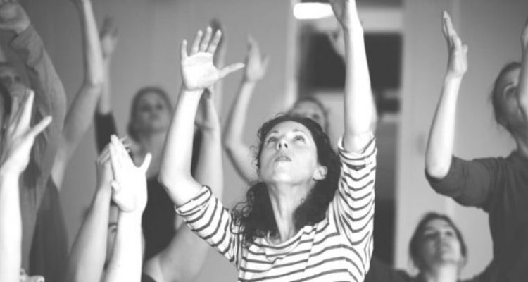 Black and white photo of Lucy among a group of dancers, lifting their arms up