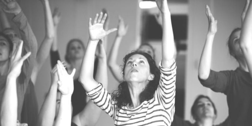 Black and white photo of Lucy among a group of dancers, lifting their arms up