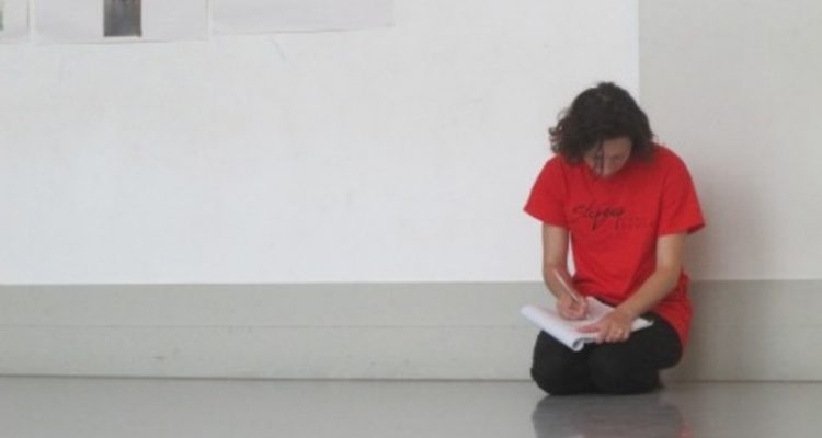 Photo of Lucy Bennett kneeling on the floor, writing into a notebook.