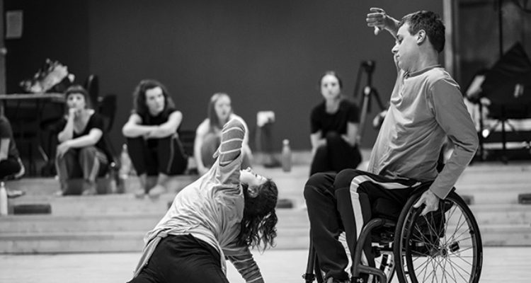 Black and white photo of a duet of a wheelchair dancer and a standing dancer.