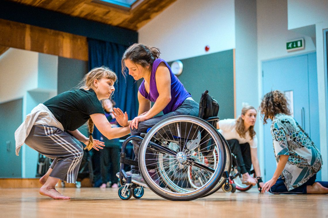 Two women dance together, one standing, one in a wheelchair.