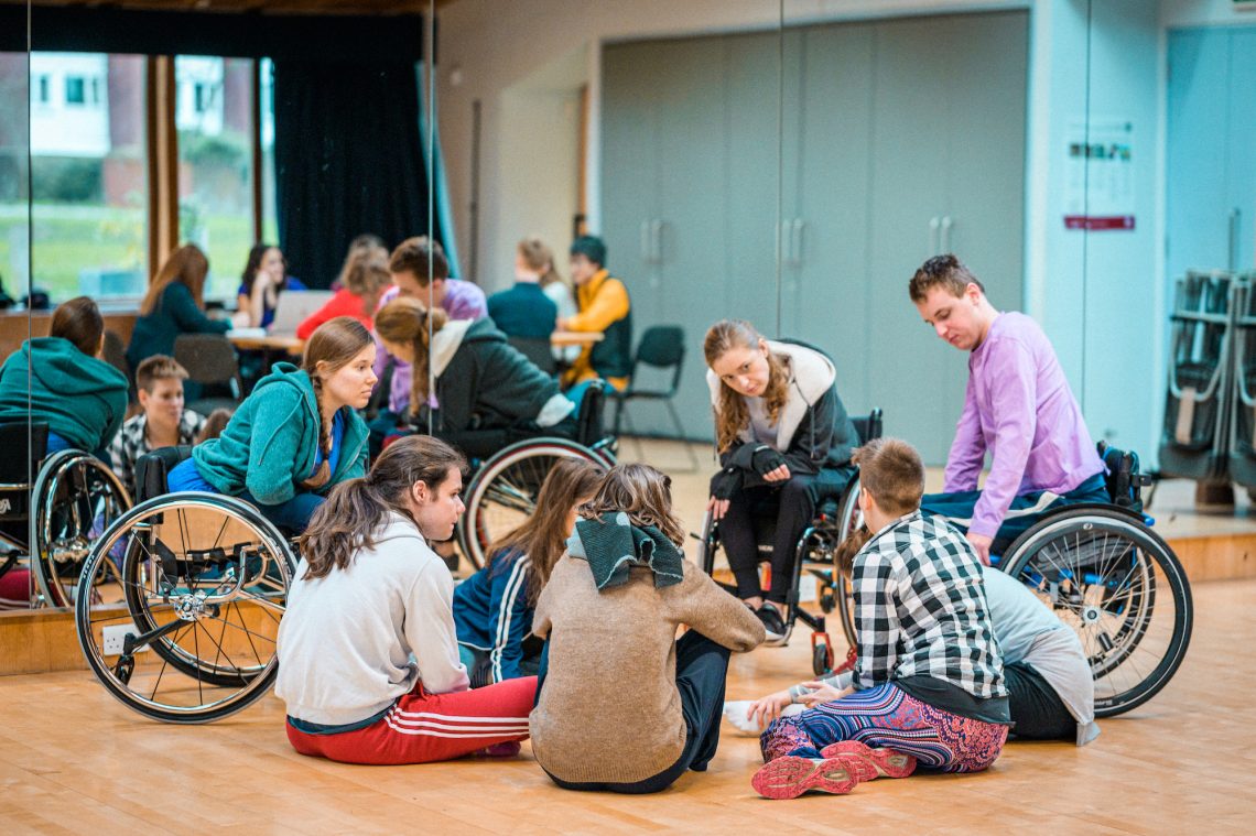 People sit talking in a circle, some on the floor, others in wheelchairs