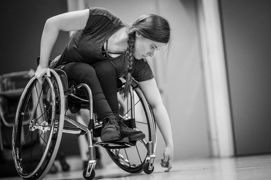 A wheelchair dancer leans down towards the floor