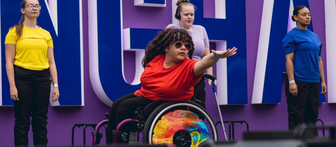 The performance at Birmingham festival. A wheelchair dancer reaches their arm forwards.
