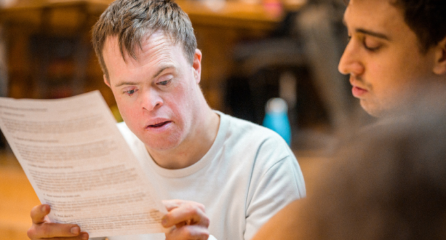 A white man with Down syndrome reads from a piece of paper.