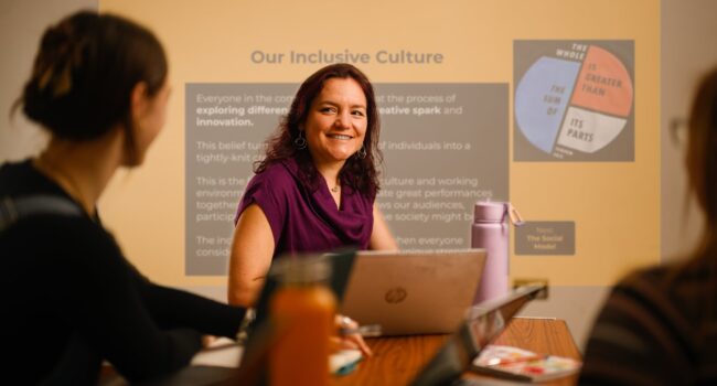 A white disabled woman in front of a powerpoint.