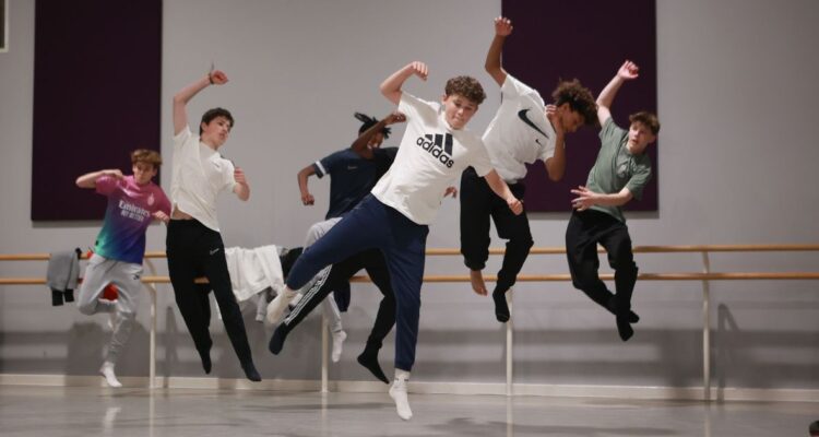 Teen male dancers leaping energetically in a studio.