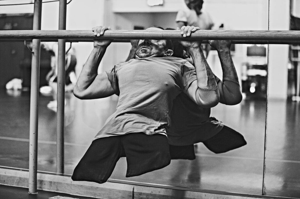 A black and white photo of Dave doing a pull-up on a ballet barre.