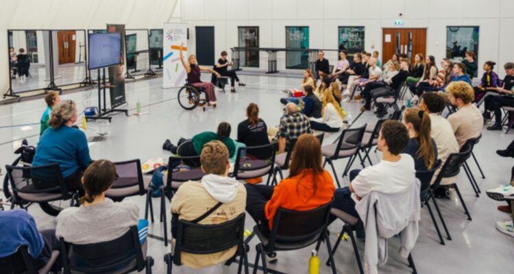 Wheelchair dancer talking to a room of seated participants Photo credit: Evan Dawson