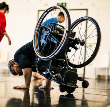 A wheelchair dancer tips to the floor with their wheels high