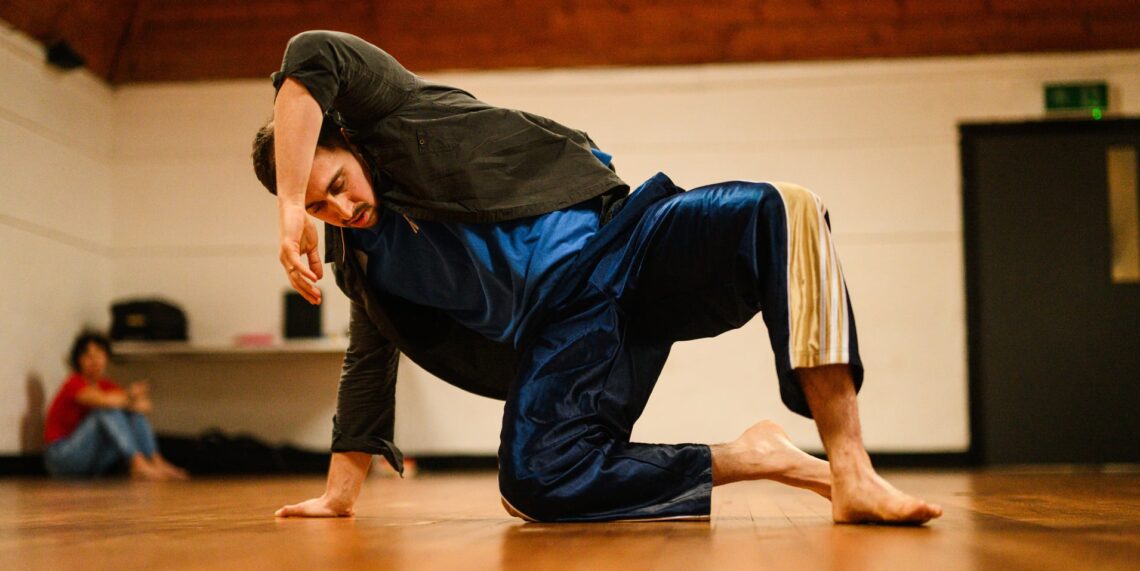 A tall white man kneels on the floor and dances.
