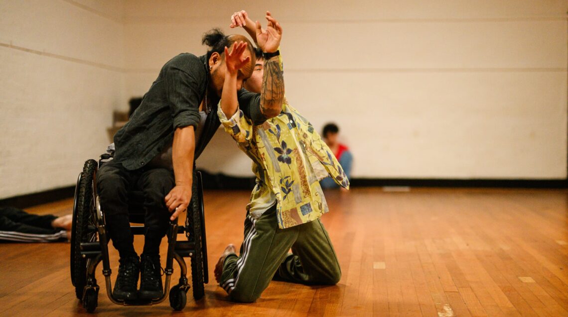 A wheelchair dancer and a standing dancer in a moment of contact.