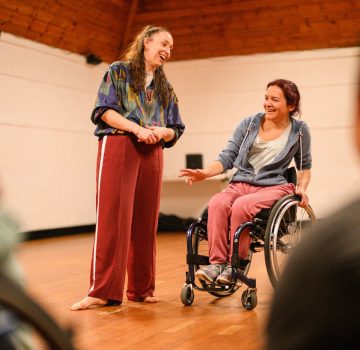 A non-disabled woman and a disabled woman speaking in front of a group.