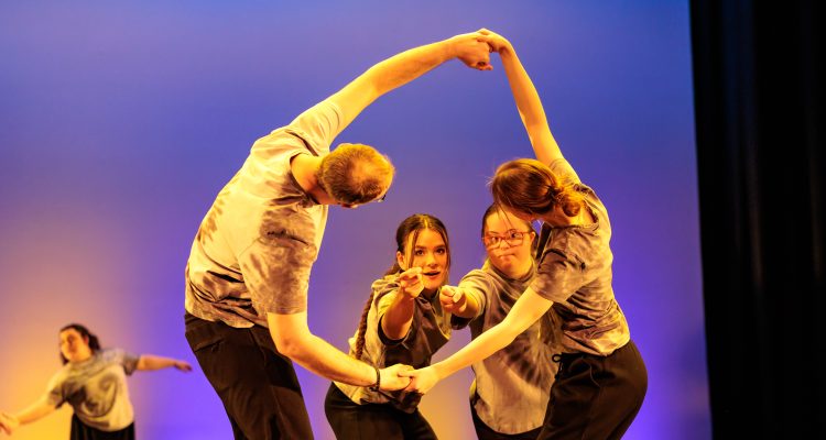 A pair of dancers looks through the gaps between another two dancers hands.