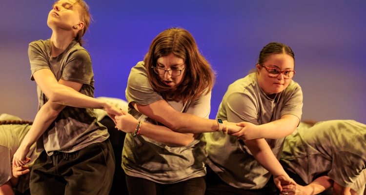 Three dancers in a line, holding hands.