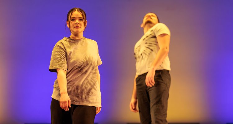 Two standing dancers, one leaning forward, the other leaning back.