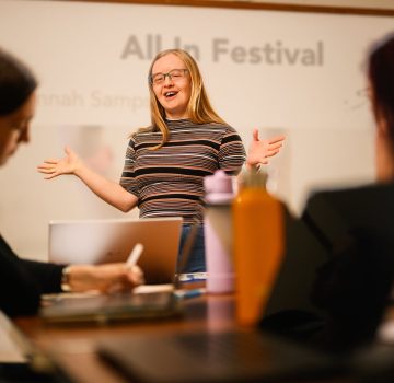 A white person with Down syndrome stands and talks to a group of people.