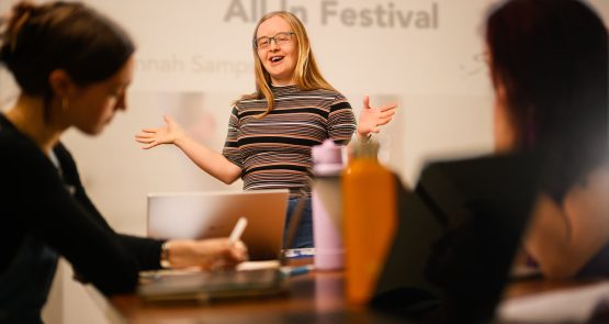 A white person with Down syndrome stands and talks to a group of people.