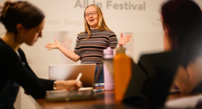 A white person with Down syndrome stands and talks to a group of people.
