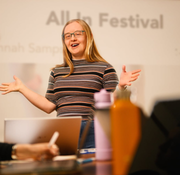 Hannah, a white person with Down syndrome stands and delivers a presentation.