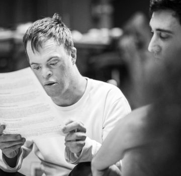 A black and white photo of a man with Down syndrome reading from a sheet of paper.