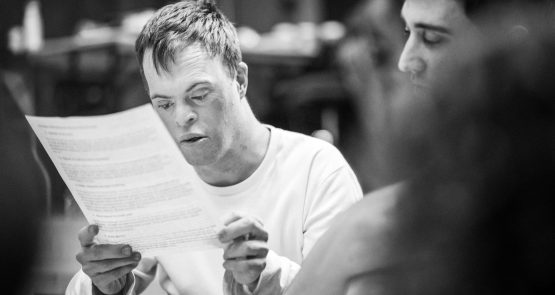 A black and white photo of a man with Down syndrome reading from a sheet of paper.