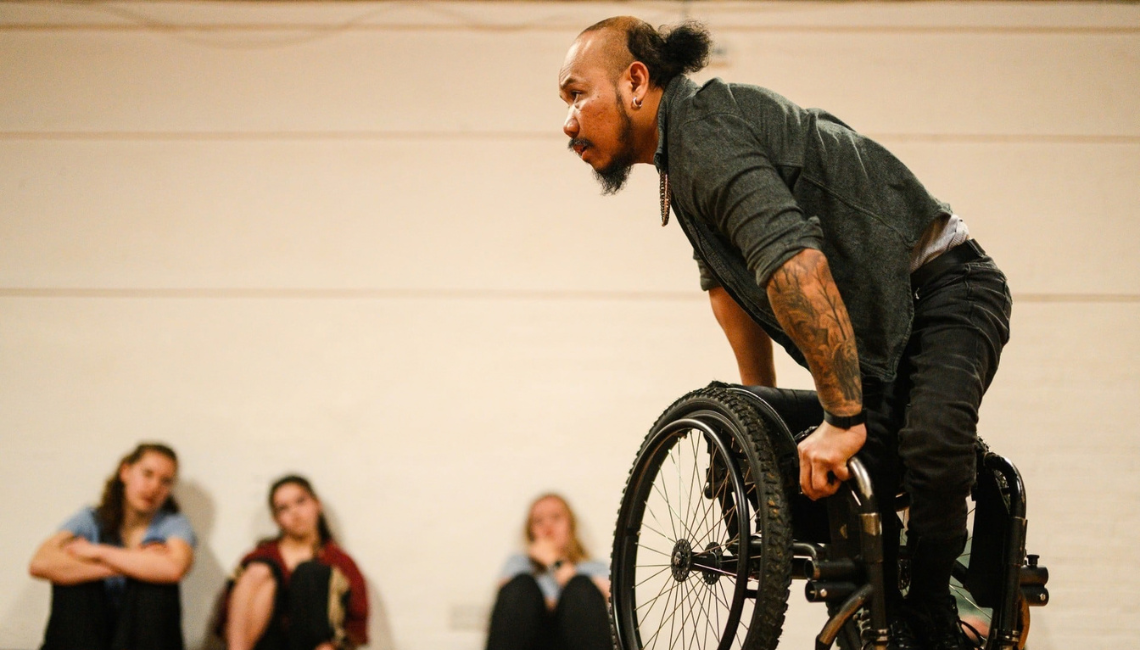 Nadenh, a British-Cambodian wheelchair dancer, pushes himself out of his chair and hovers his lower body over the seat of his manual wheelchair.